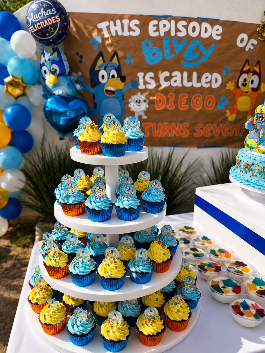 Cupcakes tematicos Bluey azul y amarillo en charola escalonada de tres pisos con paletas personalizadas y figuras de los personajes para fiesta infantil